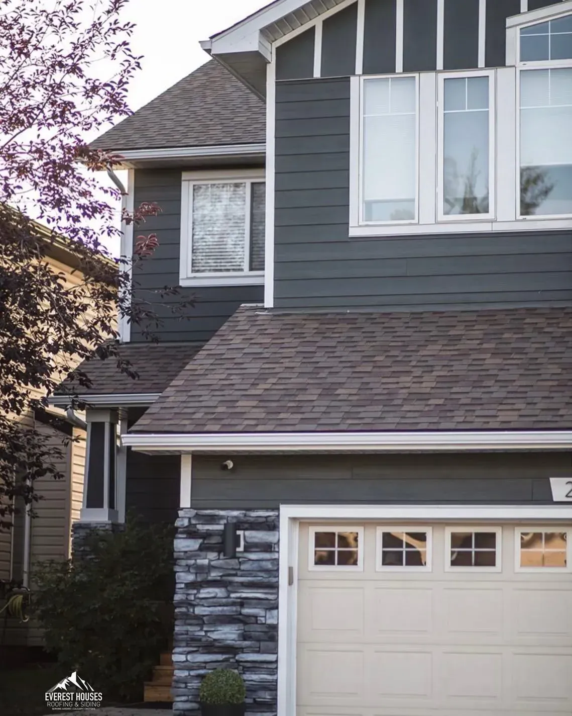 Gray two-story house with white trim, stone accents, and a beige garage door