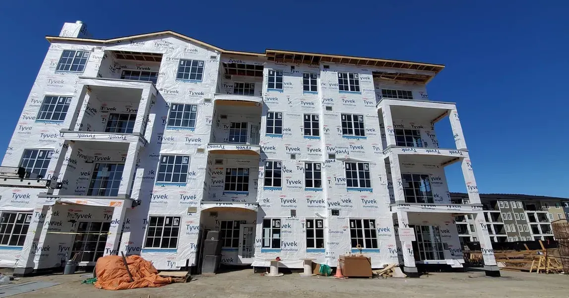Partially built white apartment building with blue window frames under a clear blue sky