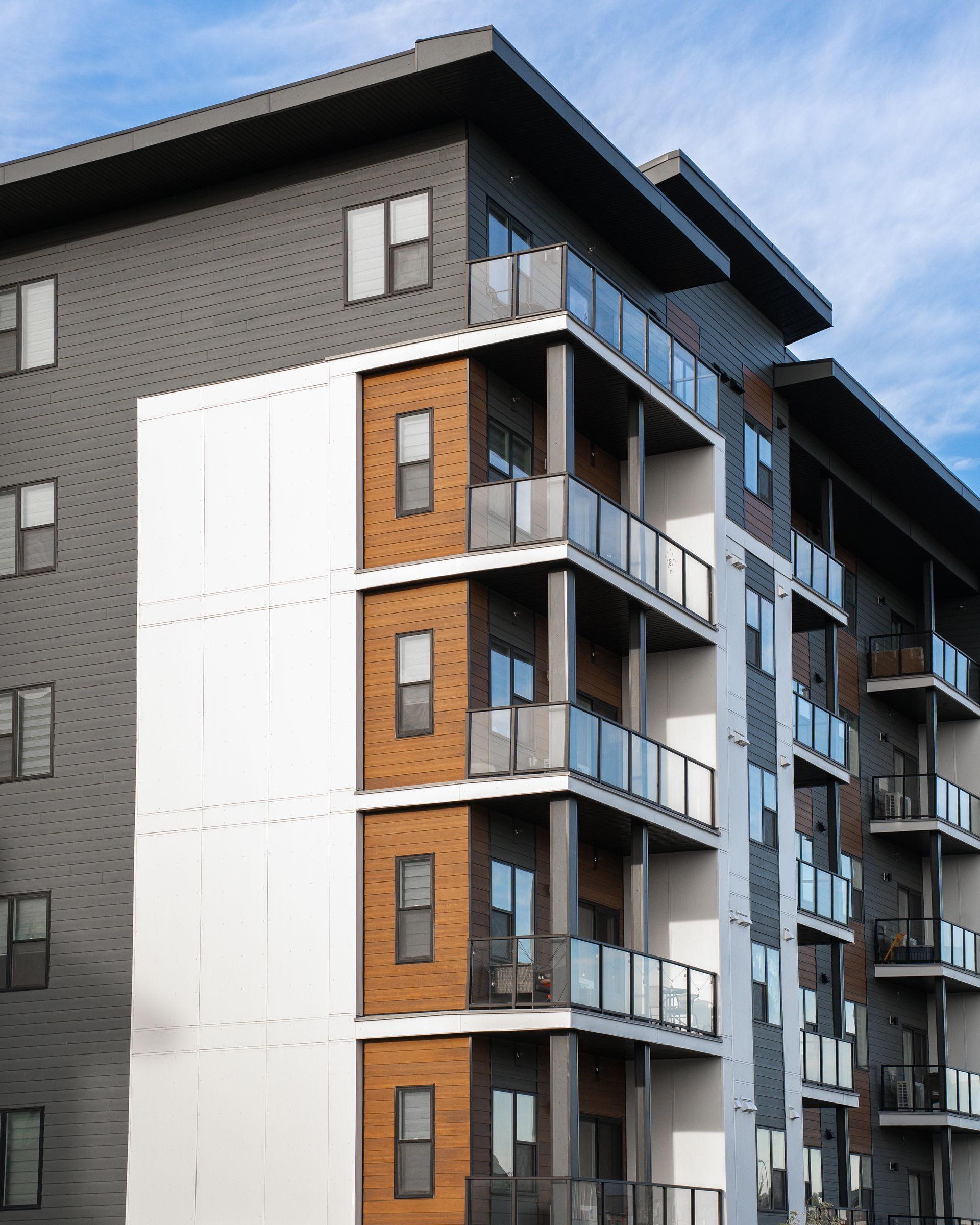 Modern apartment building with balconies and dark gray and white exterior against a blue sky Modern apartment building with balconies and dark gray and white exterior against a blue sky