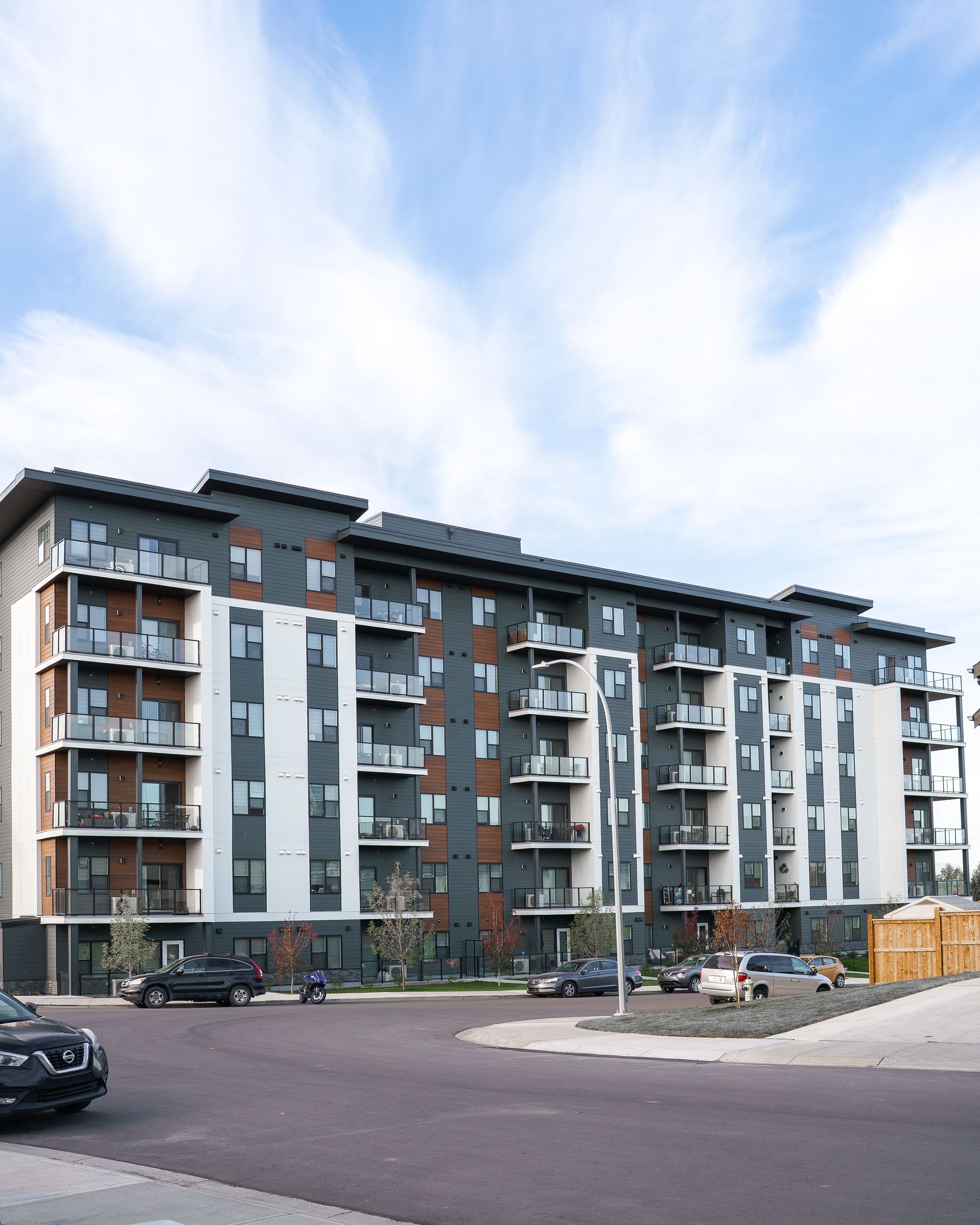 Modern apartment building with balconies and parked cars under a cloudy sky Modern apartment building with balconies and parked cars under a cloudy sky