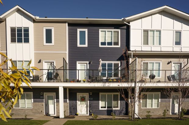 Row of modern townhouses with balconies and beige, dark gray, and white siding in daylight