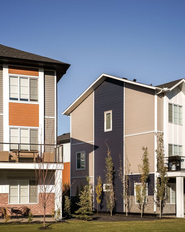 Two modern residential houses with white, orange, and dark blue siding under a clear sky