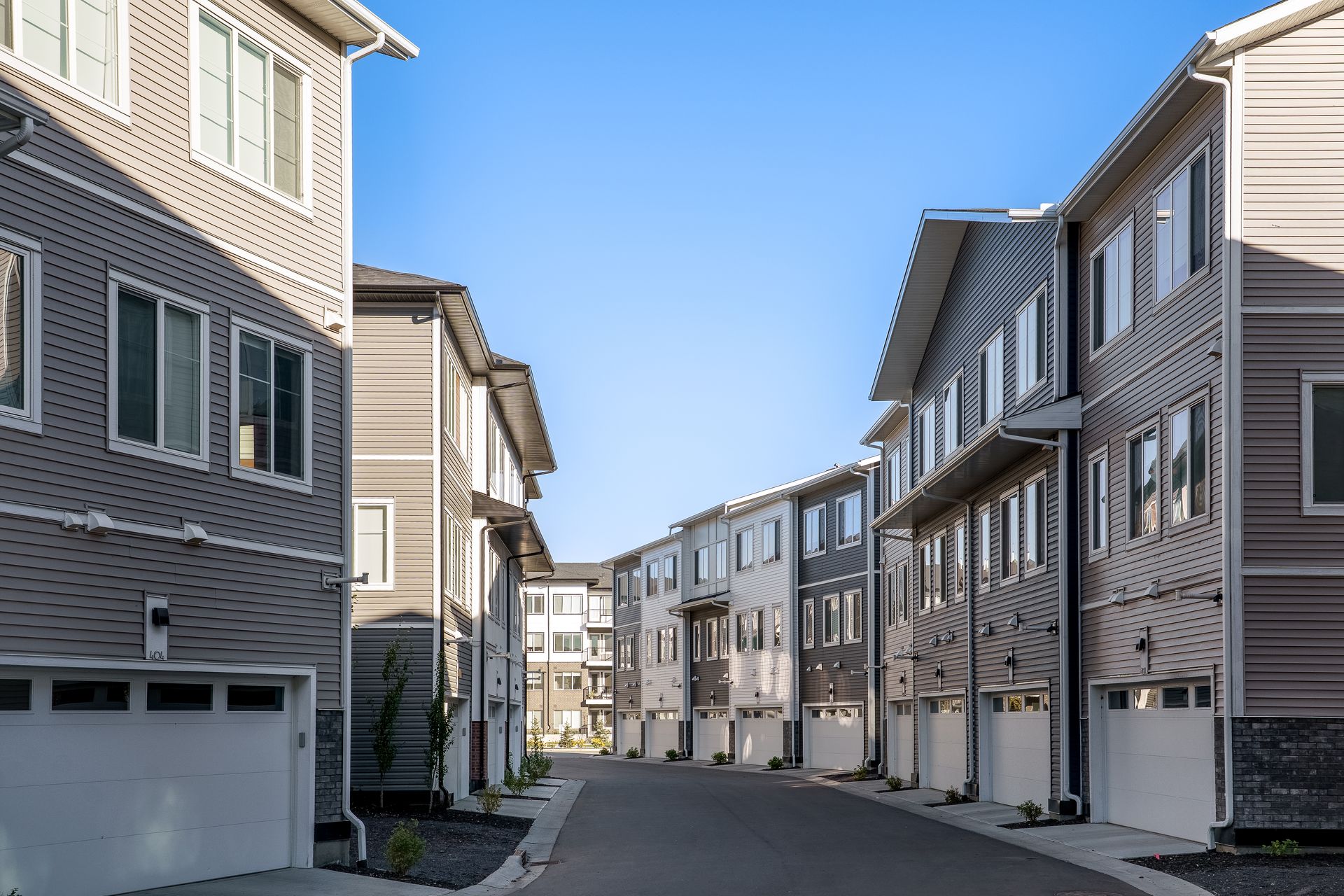 Row of modern beige townhouses along a quiet residential street under a clear blue sky Row of modern beige townhouses along a quiet residential street under a clear blue sky