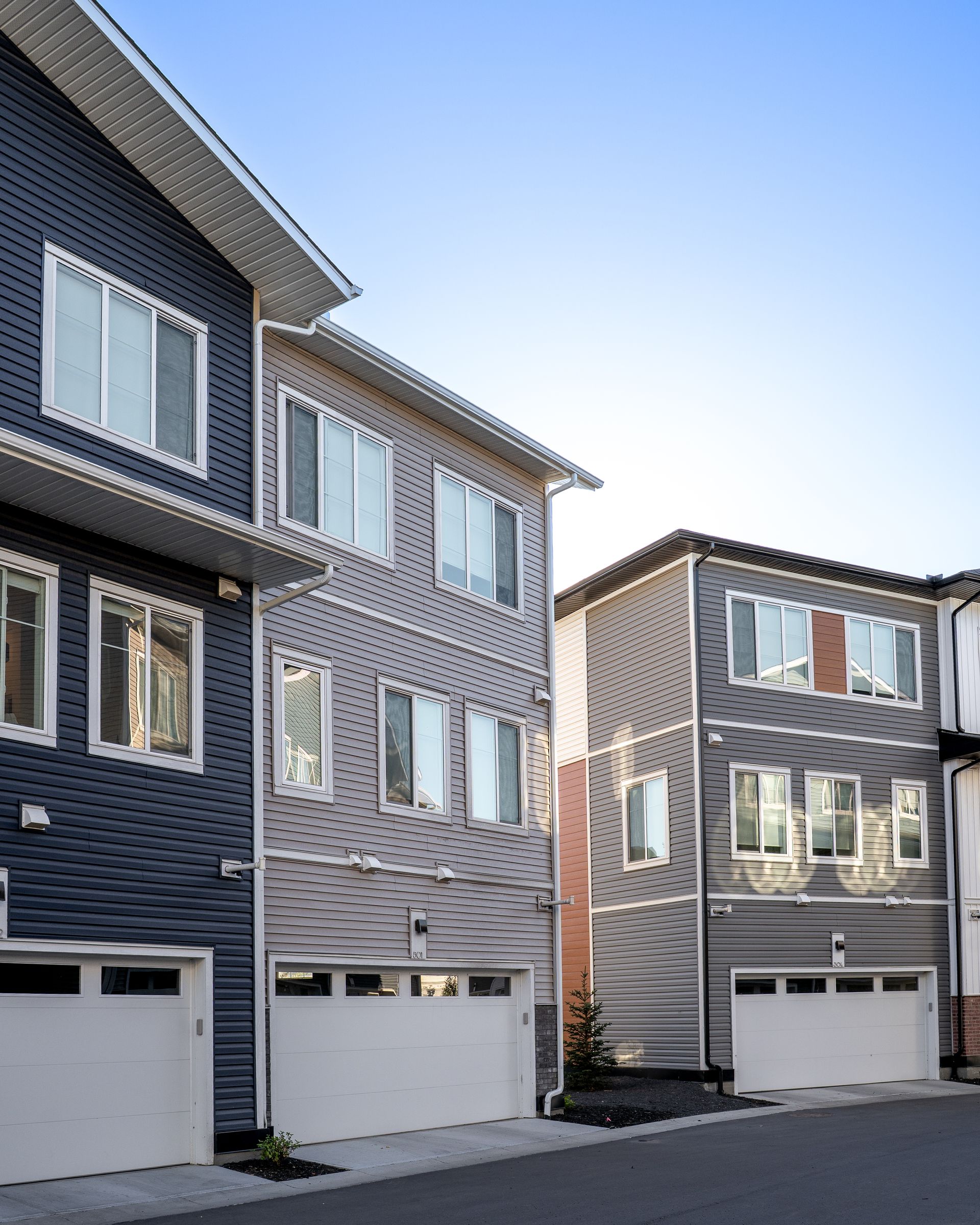 Row of gray modern townhouses with white garages under a clear blue sky Row of gray modern townhouses with white garages under a clear blue sky