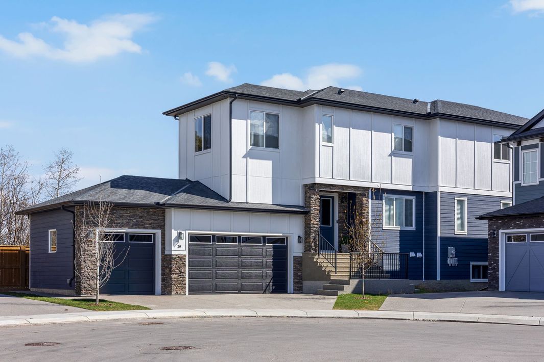 Suburban two-story house with dark gray and white exterior, garage doors, and a small front lawn under a blue sky