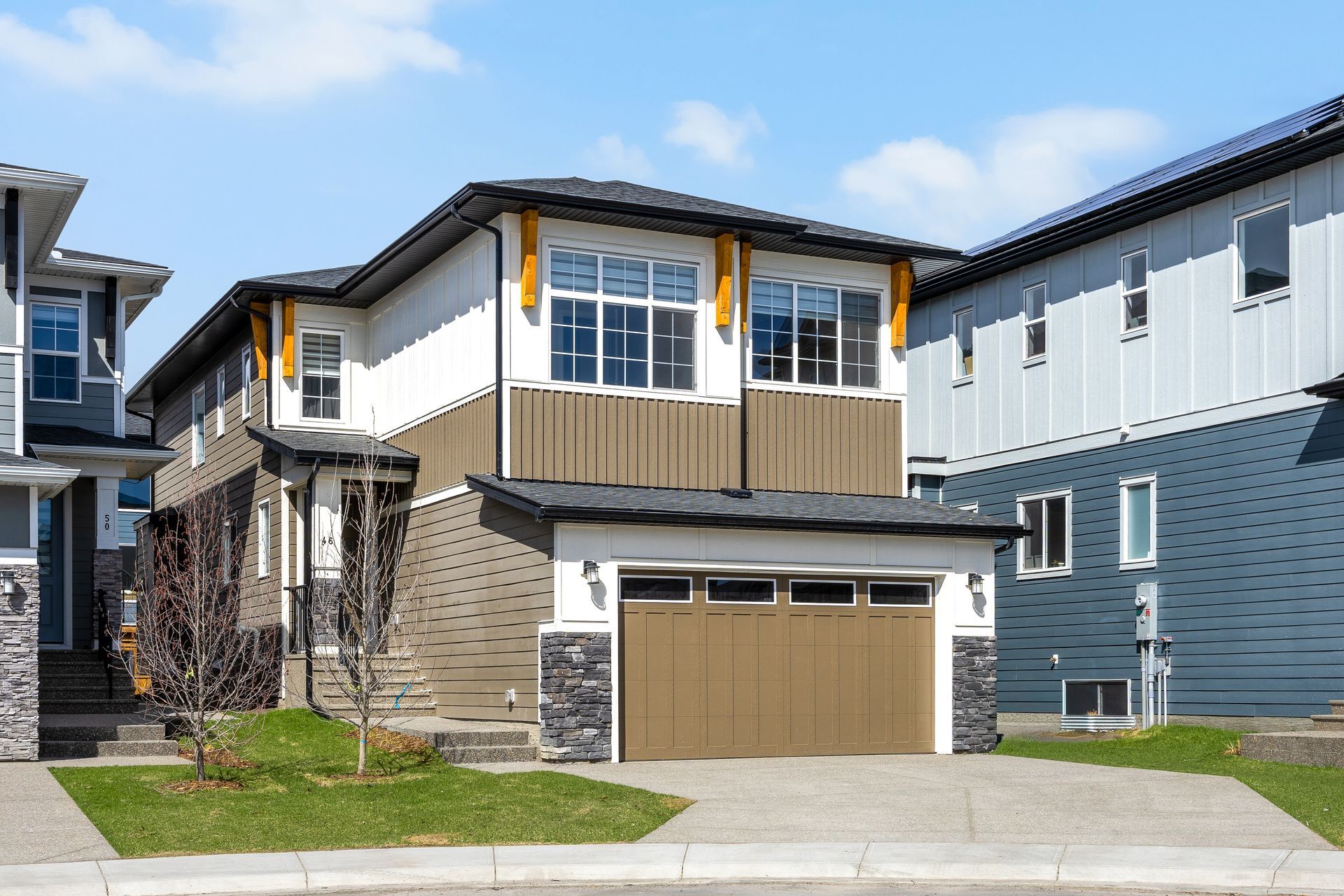 Modern two-story suburban house with tan garage doors, wood-accent balcony, and blue siding Modern two-story suburban house with tan garage doors, wood-accent balcony, and blue siding