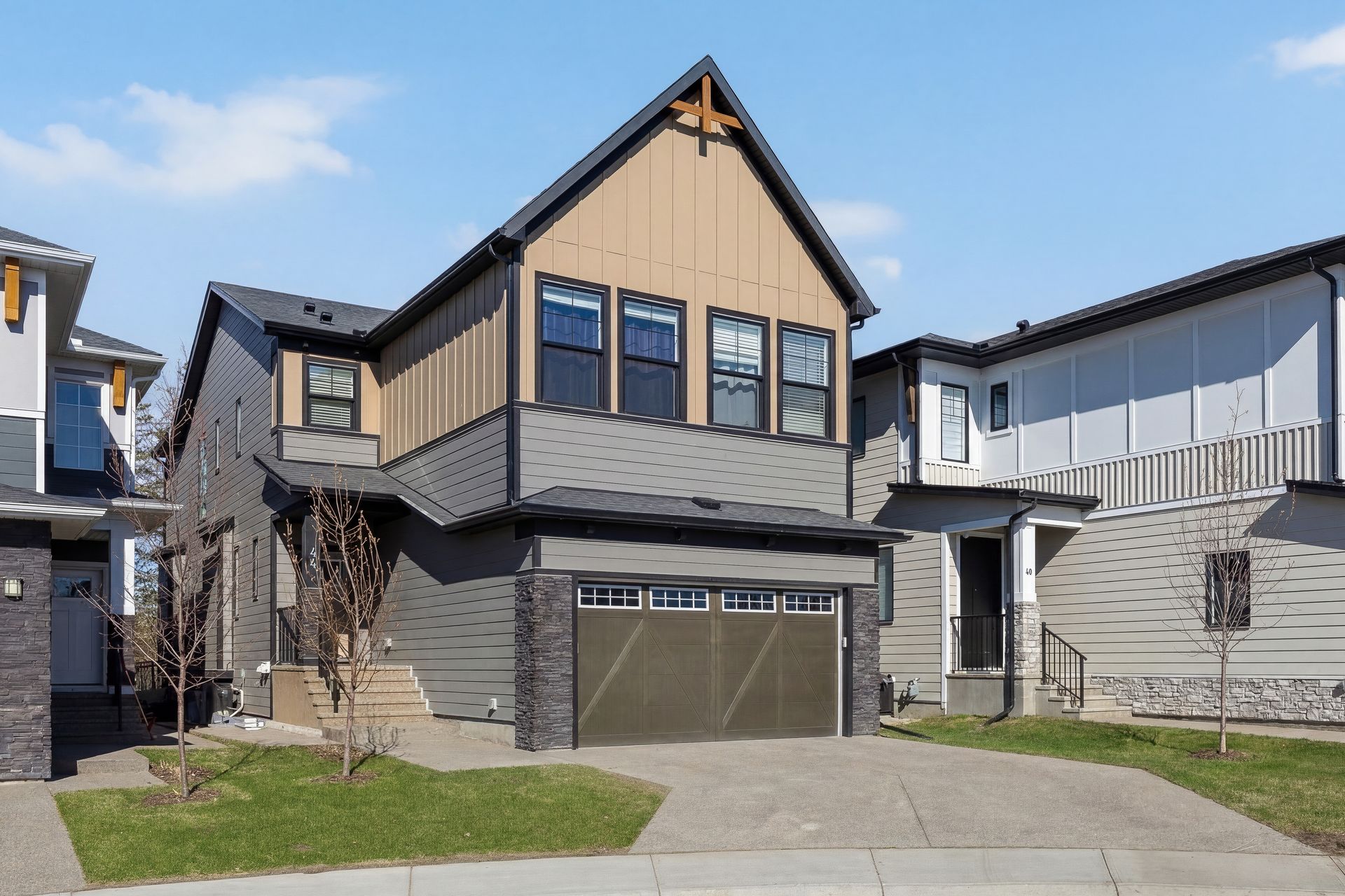 Modern two-story house with beige siding, stone accents, and a double garage on a suburban street Modern two-story house with beige siding, stone accents, and a double garage on a suburban street