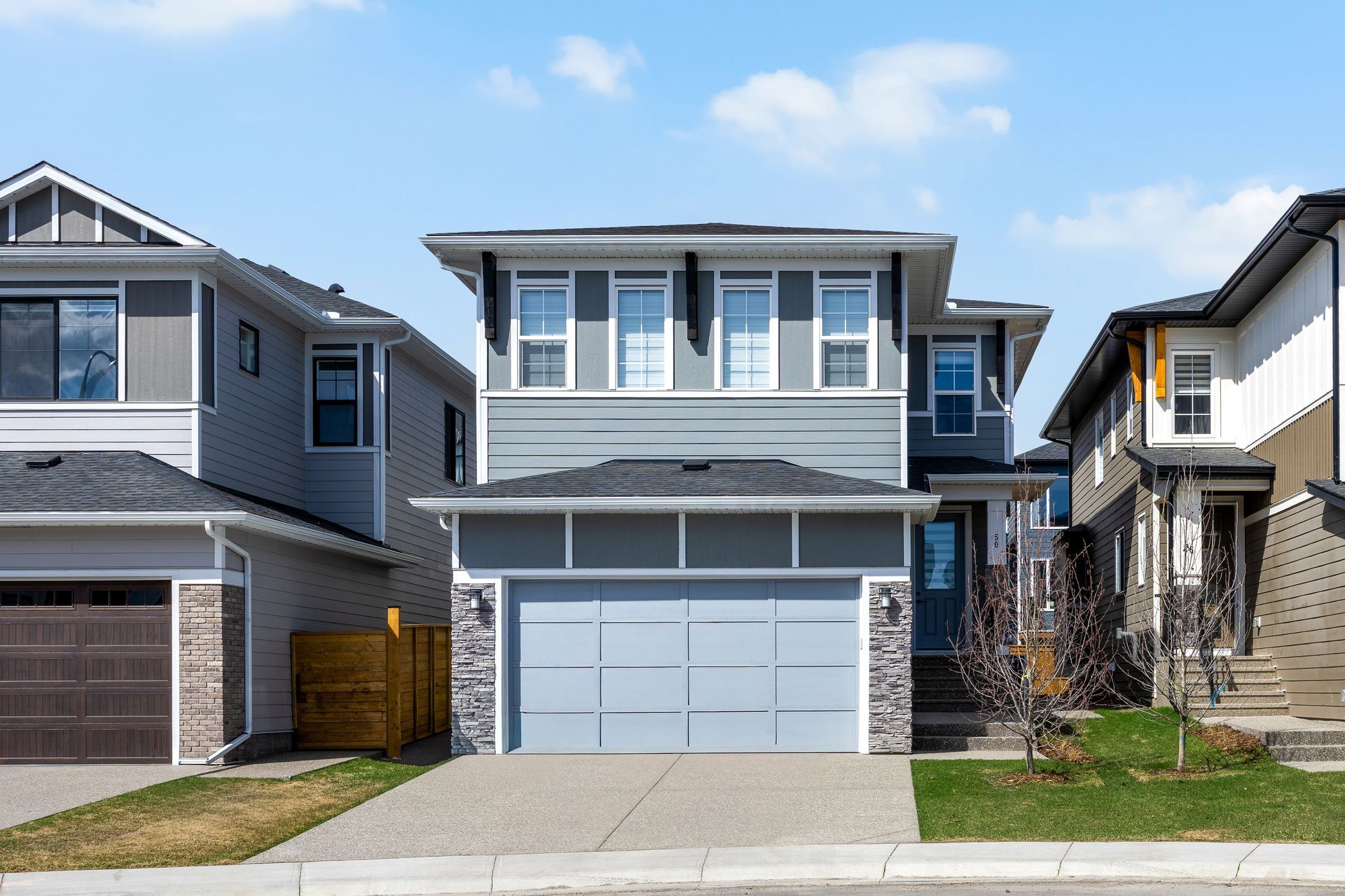 Two-story suburban house with a gray exterior, attached garage, and driveway under a blue sky. Two-story suburban house with a gray exterior, attached garage, and driveway under a blue sky.