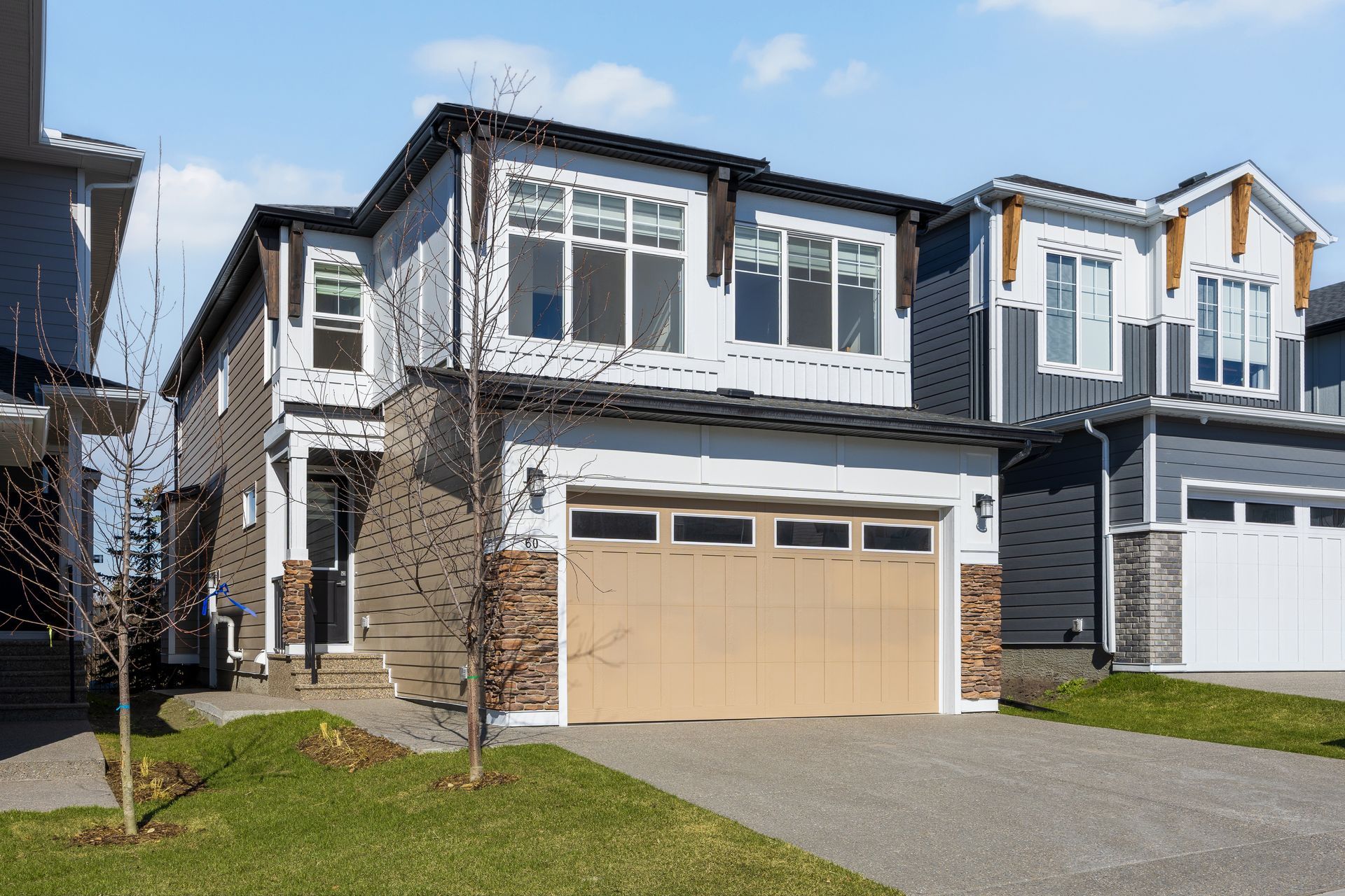 Modern two-story suburban house with beige garage, white trim, and a green lawn under a blue sky Modern two-story suburban house with beige garage, white trim, and a green lawn under a blue sky