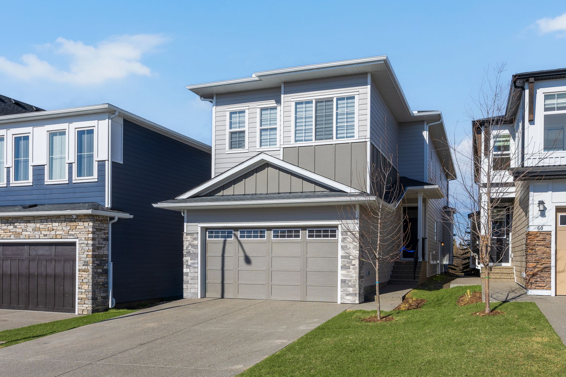 Suburban two-story house with gray garage doors, blue siding, and a driveway under bright sun Suburban two-story house with gray garage doors, blue siding, and a driveway under bright sun