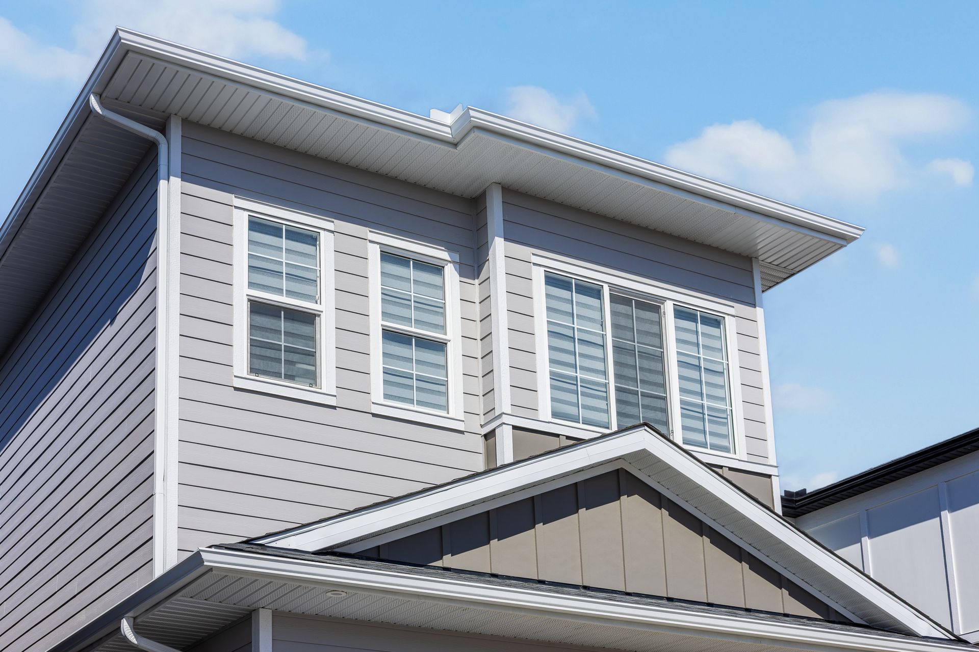 Two-story house with light gray siding, white-trim windows, and a blue sky background Two-story house with light gray siding, white-trim windows, and a blue sky background