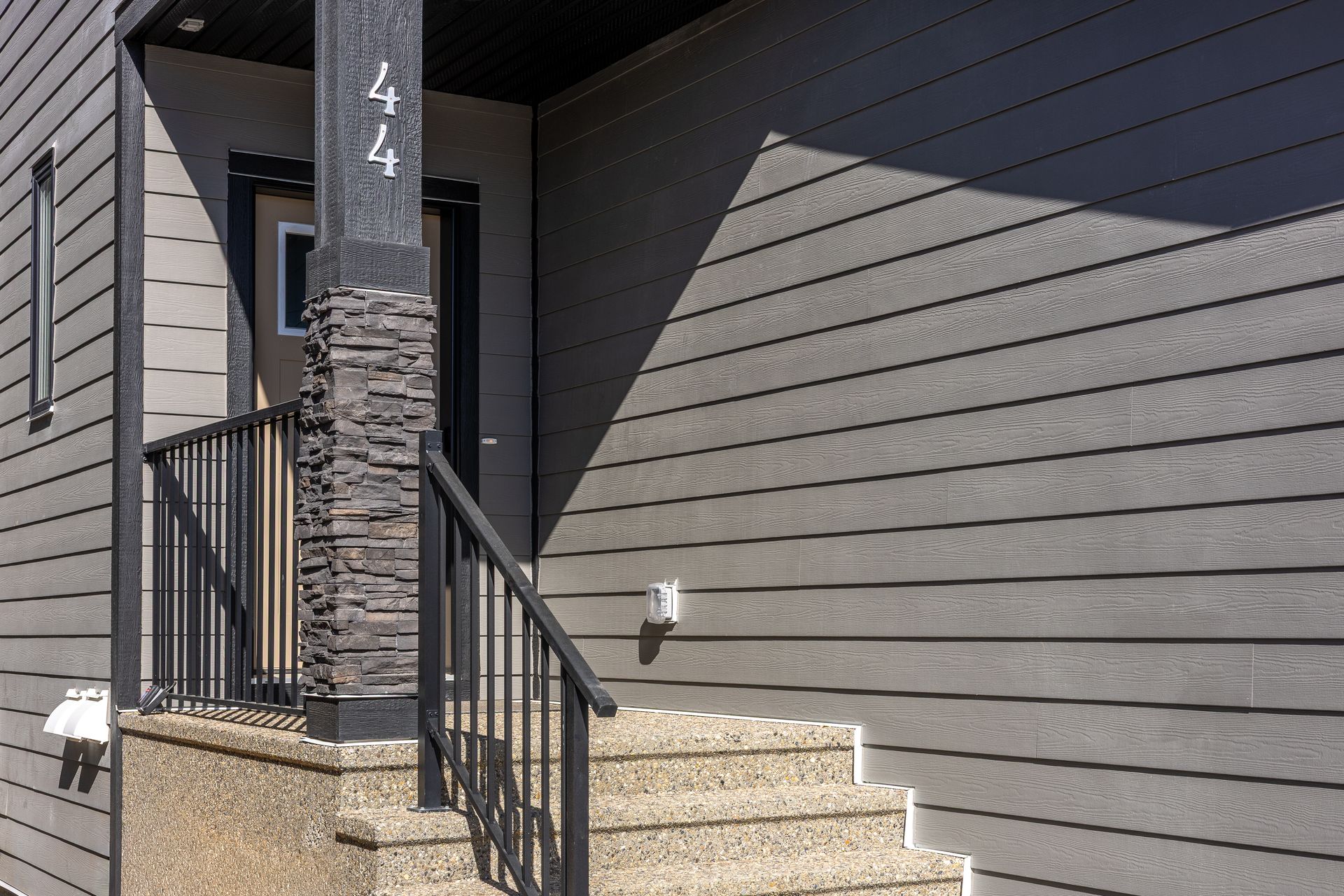 Front steps with metal railing leading to a gray house entrance beside a stone pillar marked 44 Front steps with metal railing leading to a gray house entrance beside a stone pillar marked 44