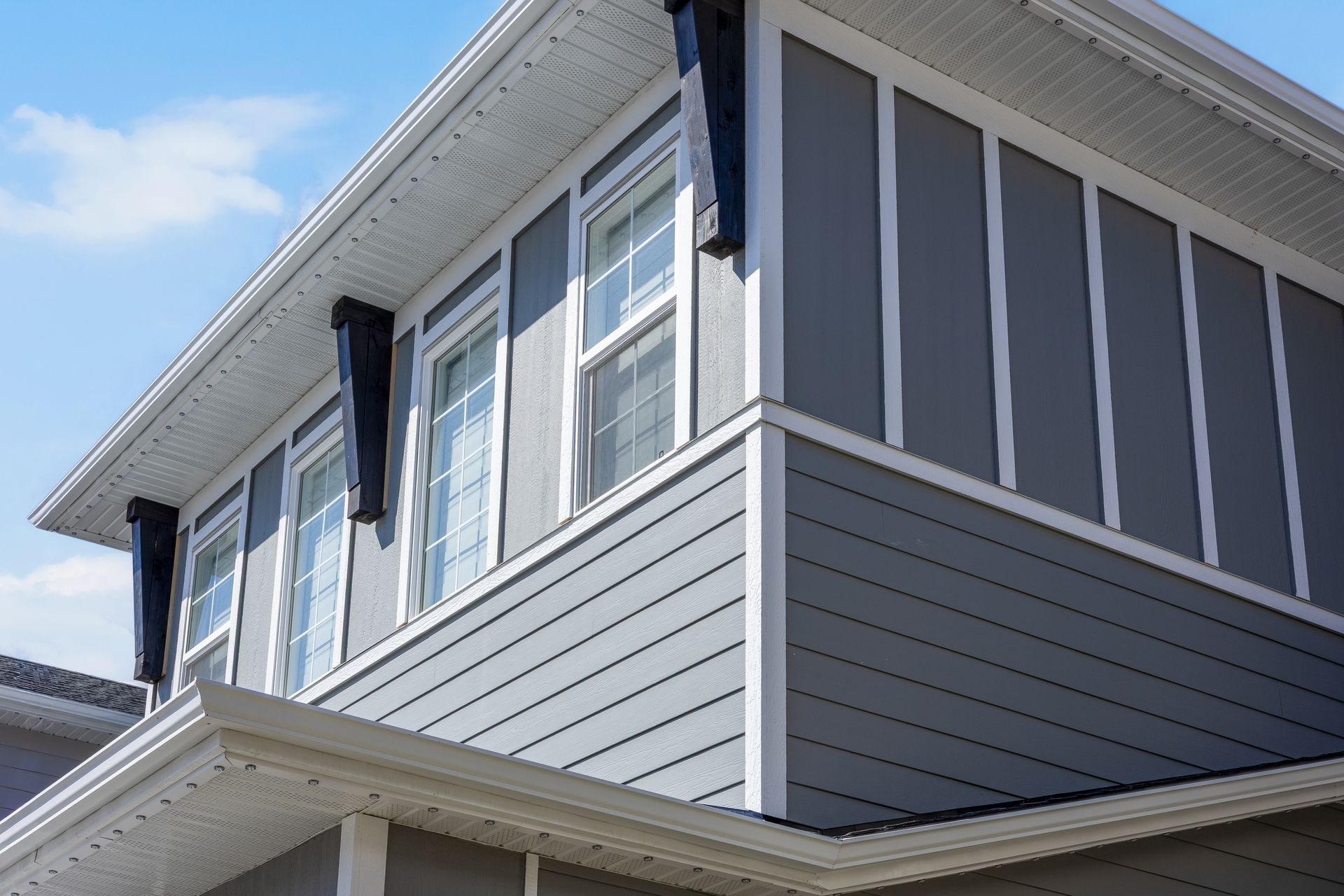 Corner of a two-story house with gray siding and white trim against a blue sky Corner of a two-story house with gray siding and white trim against a blue sky
