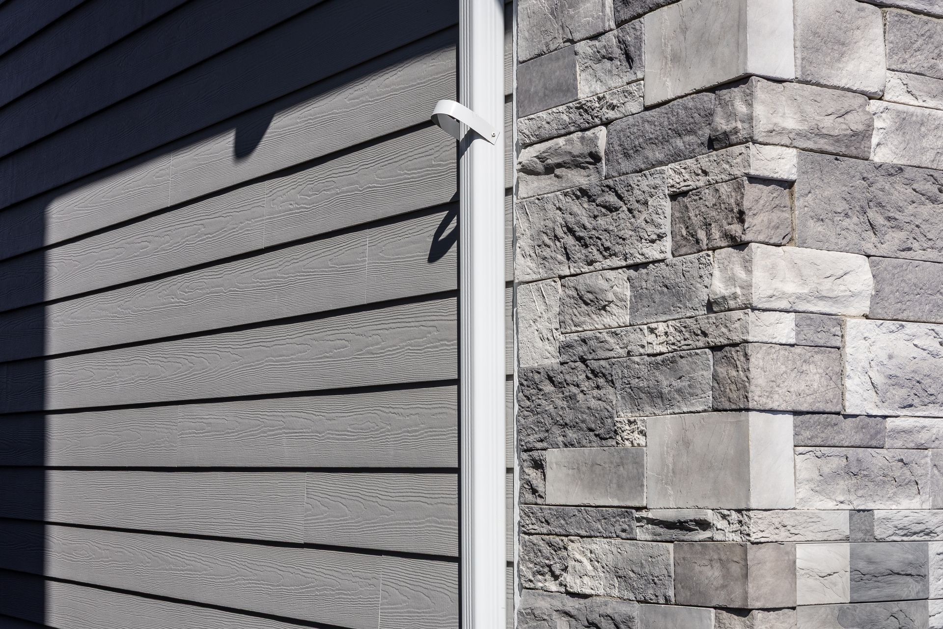 Exterior corner of a house with gray siding meeting a stone wall and white trim Exterior corner of a house with gray siding meeting a stone wall and white trim
