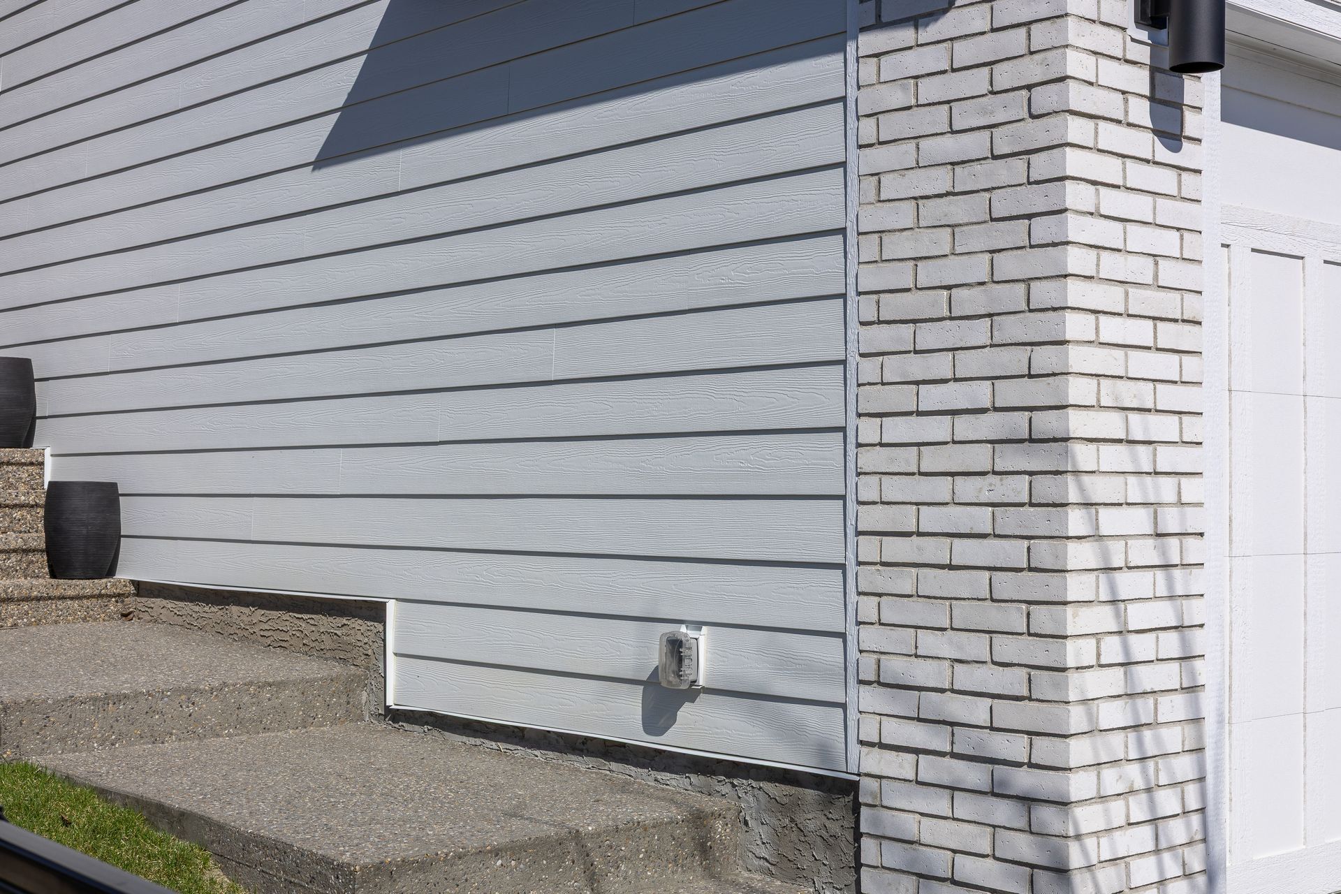 Gray house exterior with white brick corner, siding, and gravel ground beside a fence Gray house exterior with white brick corner, siding, and gravel ground beside a fence