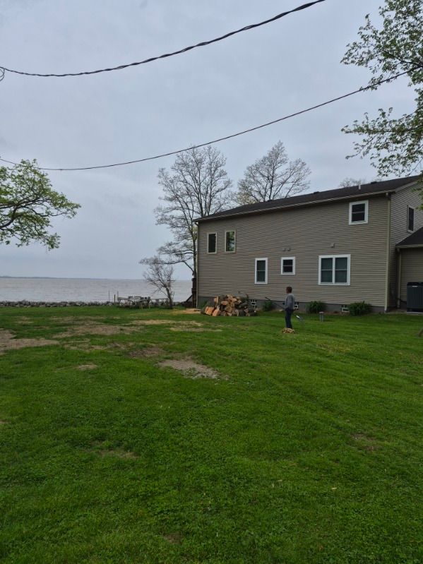 Grassy yard by a lakeside house under gray skies, with a person near the deck and trees in the background