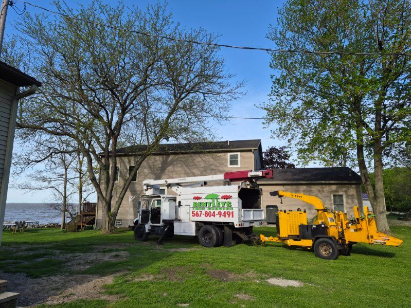 White truck and yellow wood chipper by a house near the water on a grassy yard