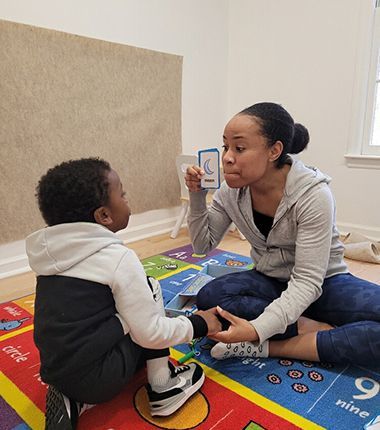 Woman showing a card with a crescent moon to a child sitting on a colorful mat.