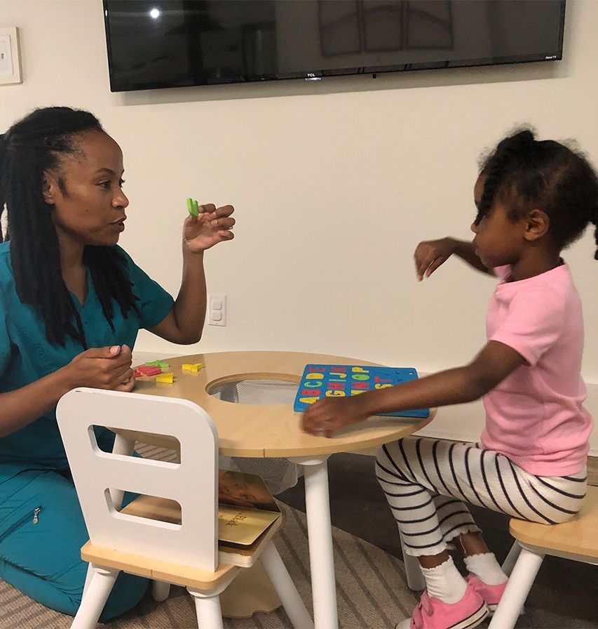 Therapist showing object to child at table in a therapy room.