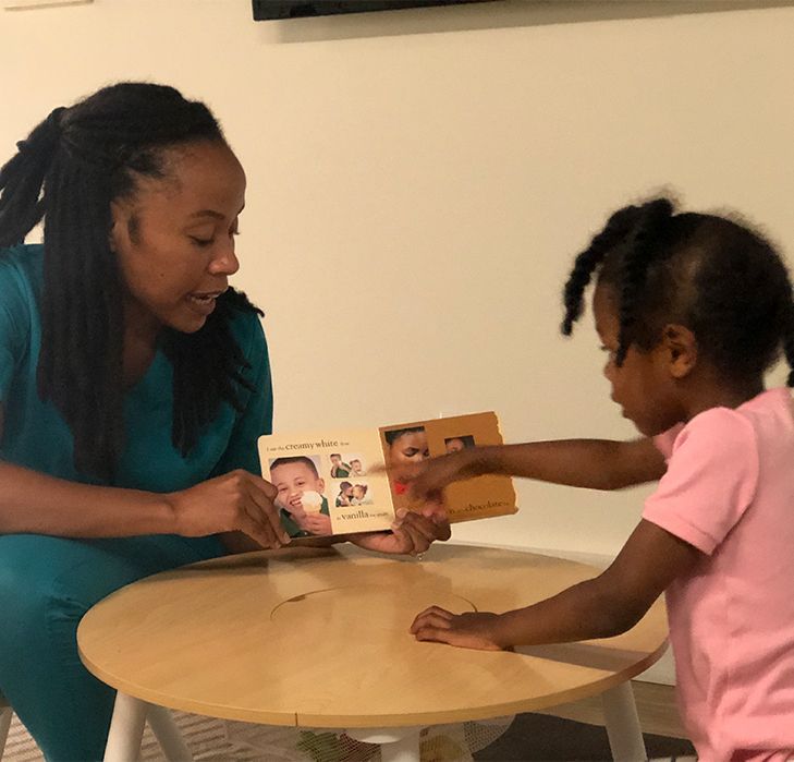 Woman and young child looking at a book together at a small table. Woman points to the book.