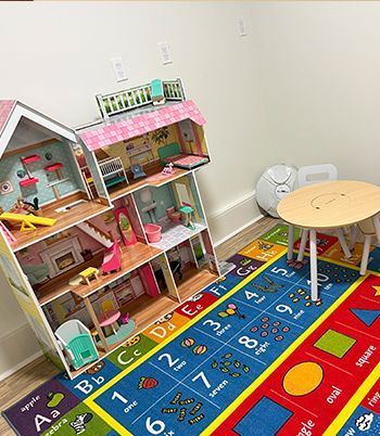 Dollhouse and small table with chairs on a colorful alphabet rug in a playroom.
