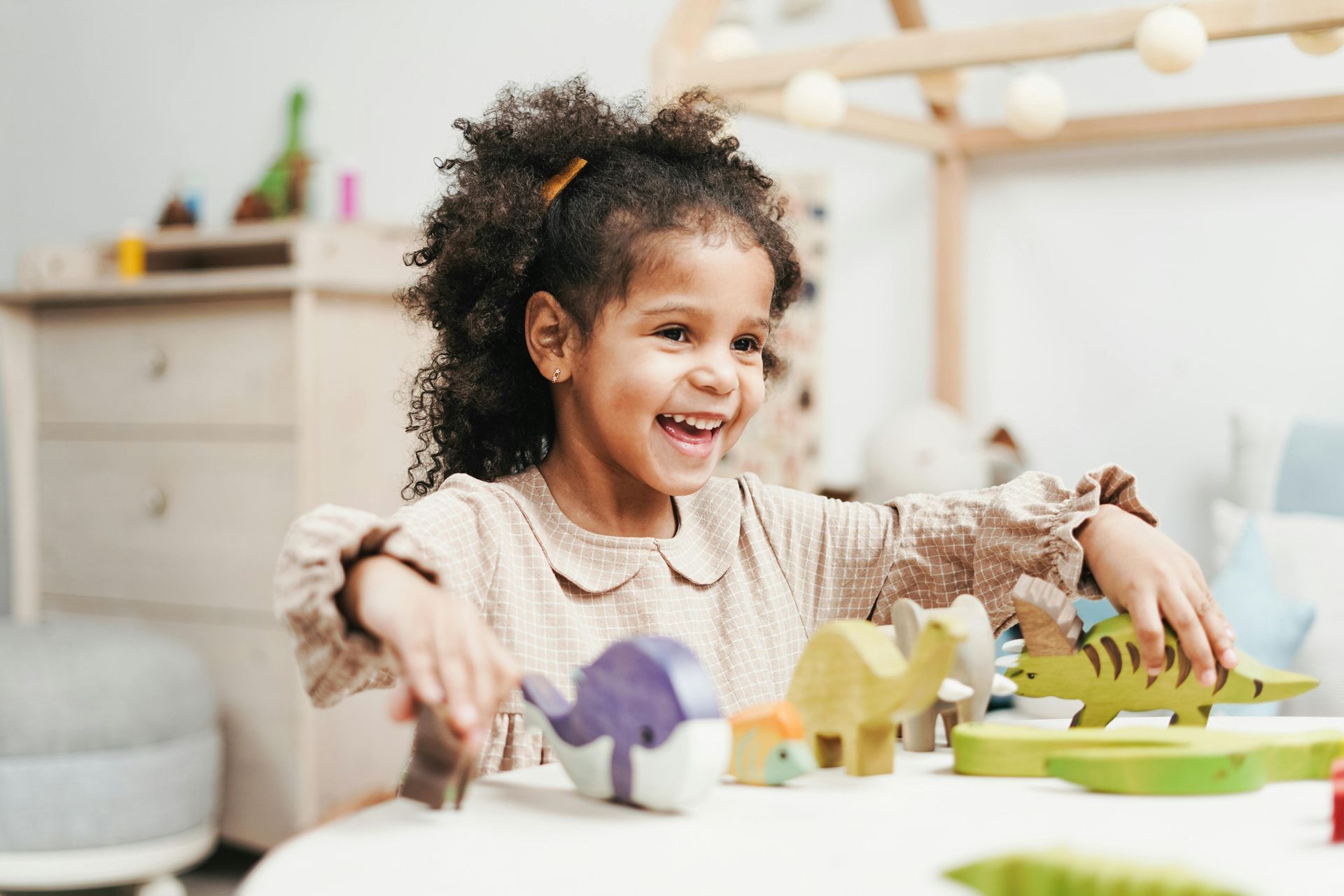 Girl playing with colorful wooden toys, smiling joyfully at a table in a bright room.