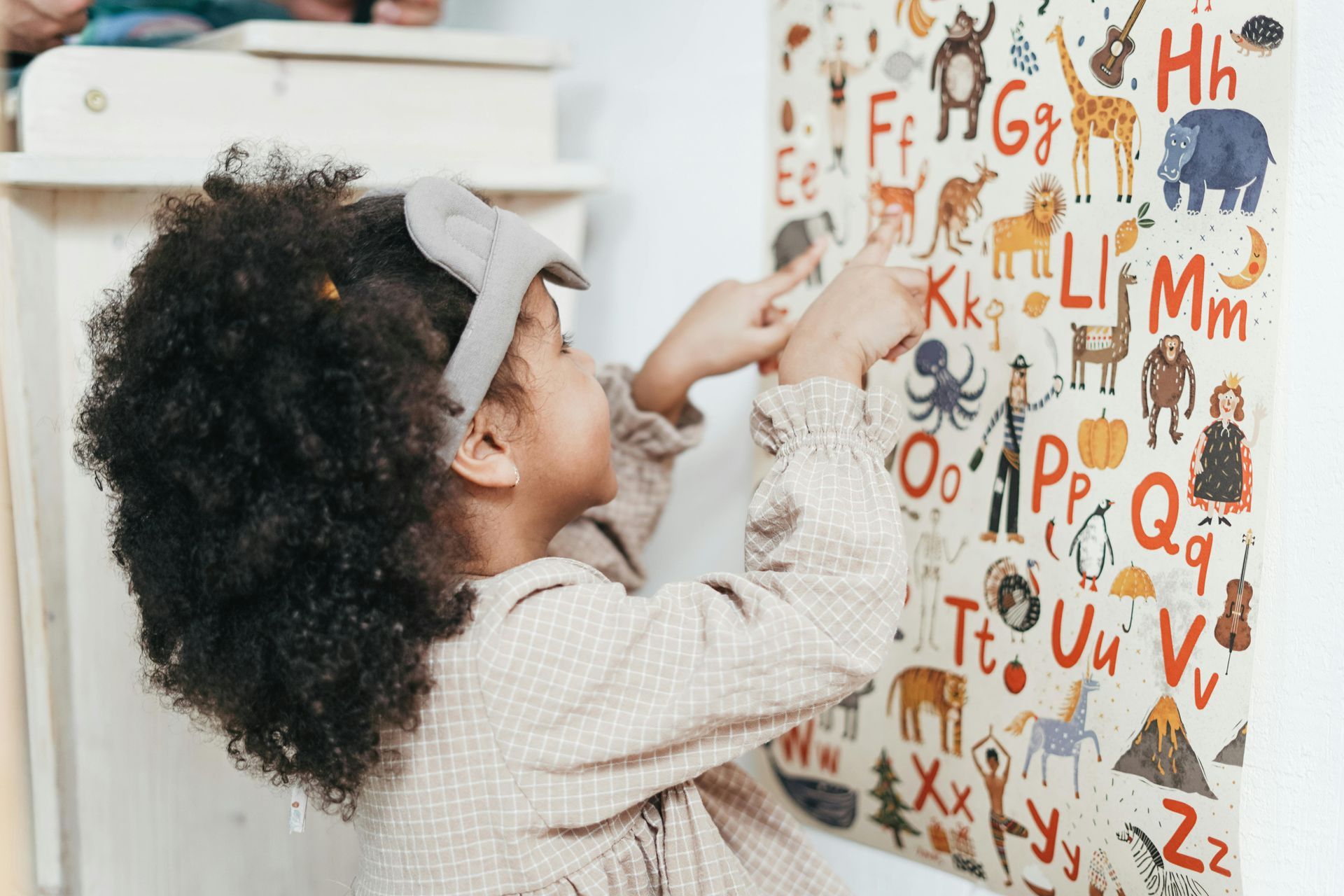 Child points at alphabet chart on wall.
