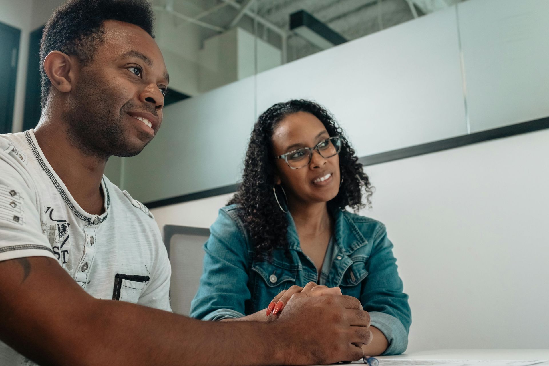 Two people, one wearing a patterned shirt, the other a denim jacket, in discussion at a table.
