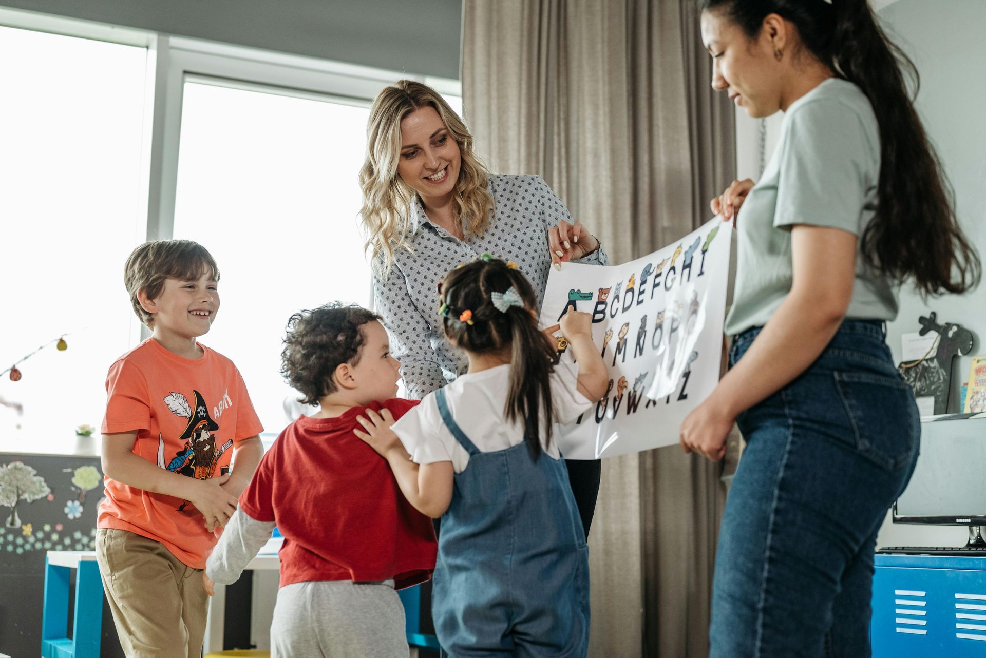 Two teachers show a chart to four children in a classroom.