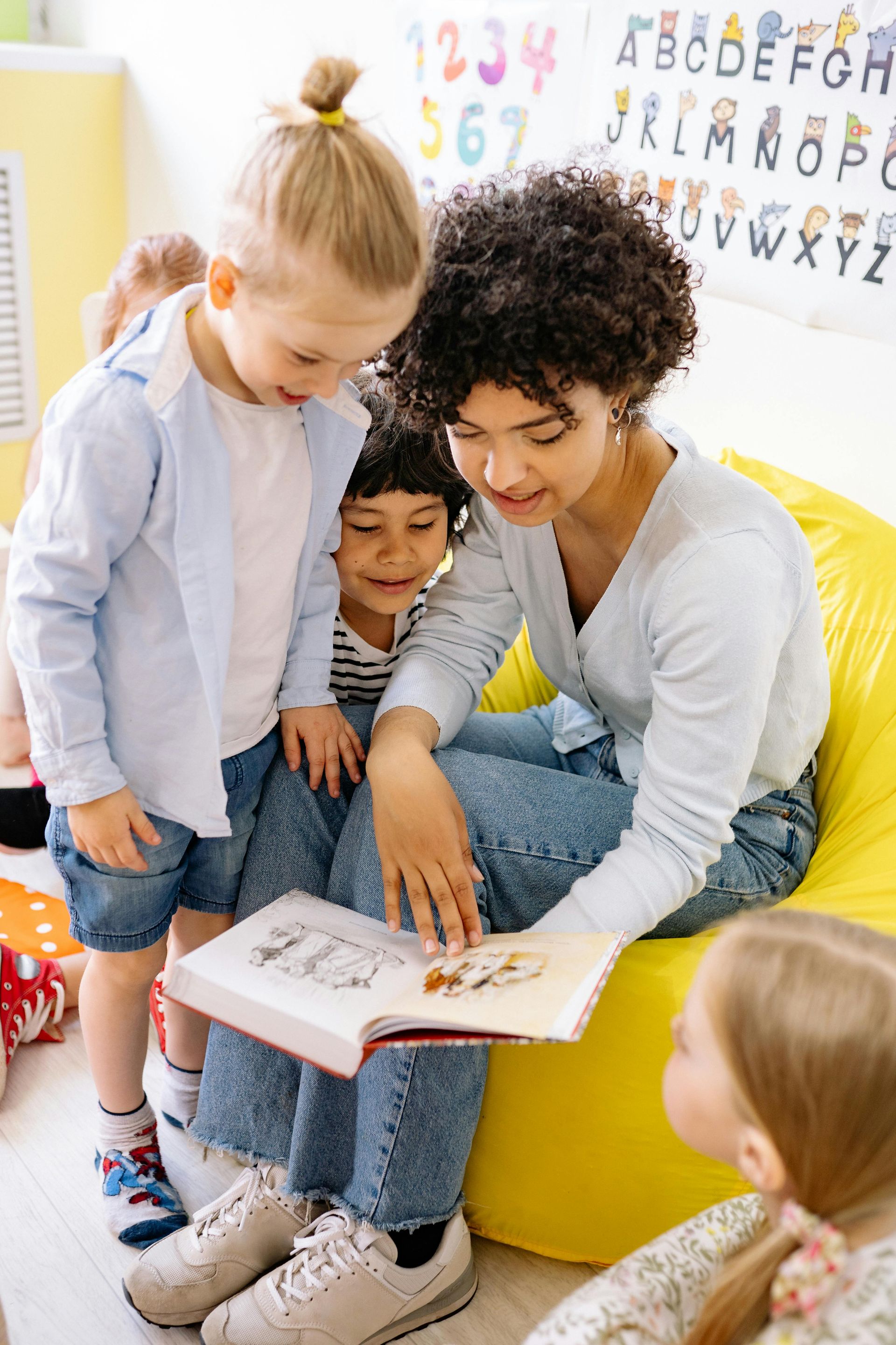 Teacher reading a book to a group of children in a classroom.