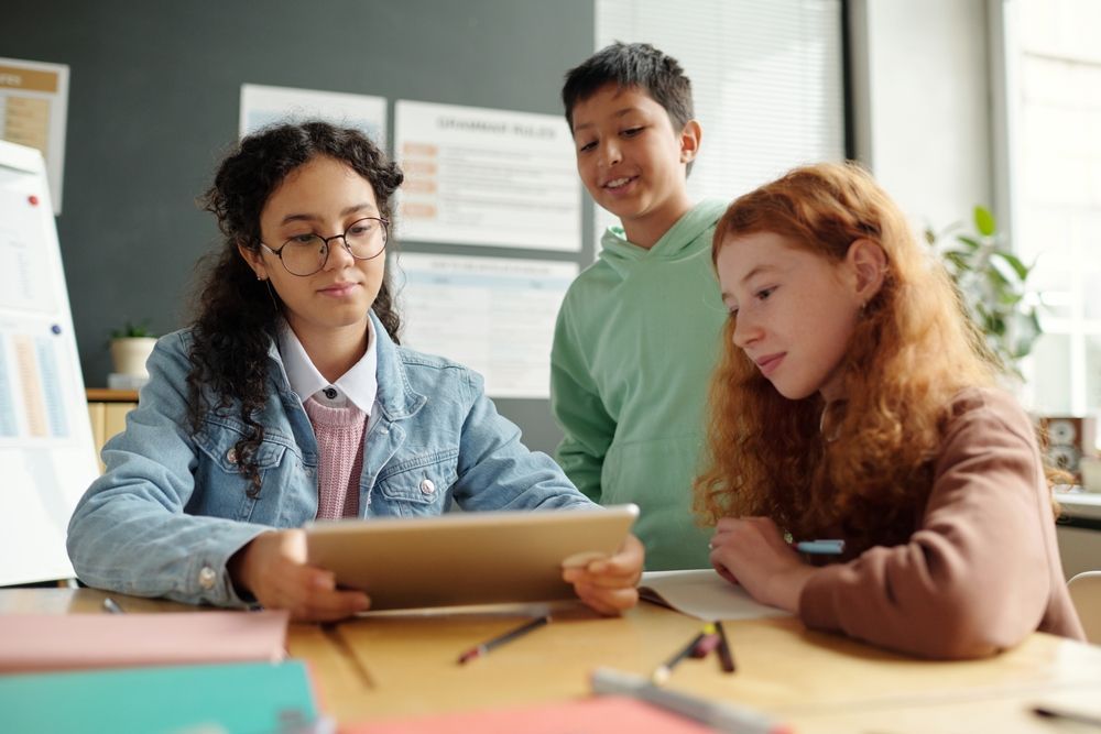 Three students looking at a tablet together in a classroom.