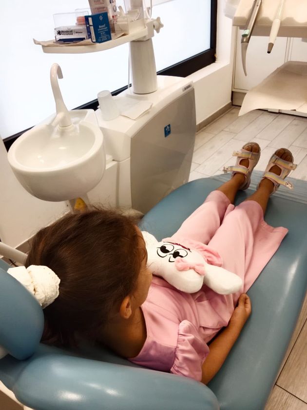 Bambino sdraiato su una poltrona odontoiatrica durante una visita, con lavandino e attrezzature dentistiche nelle vicinanze.