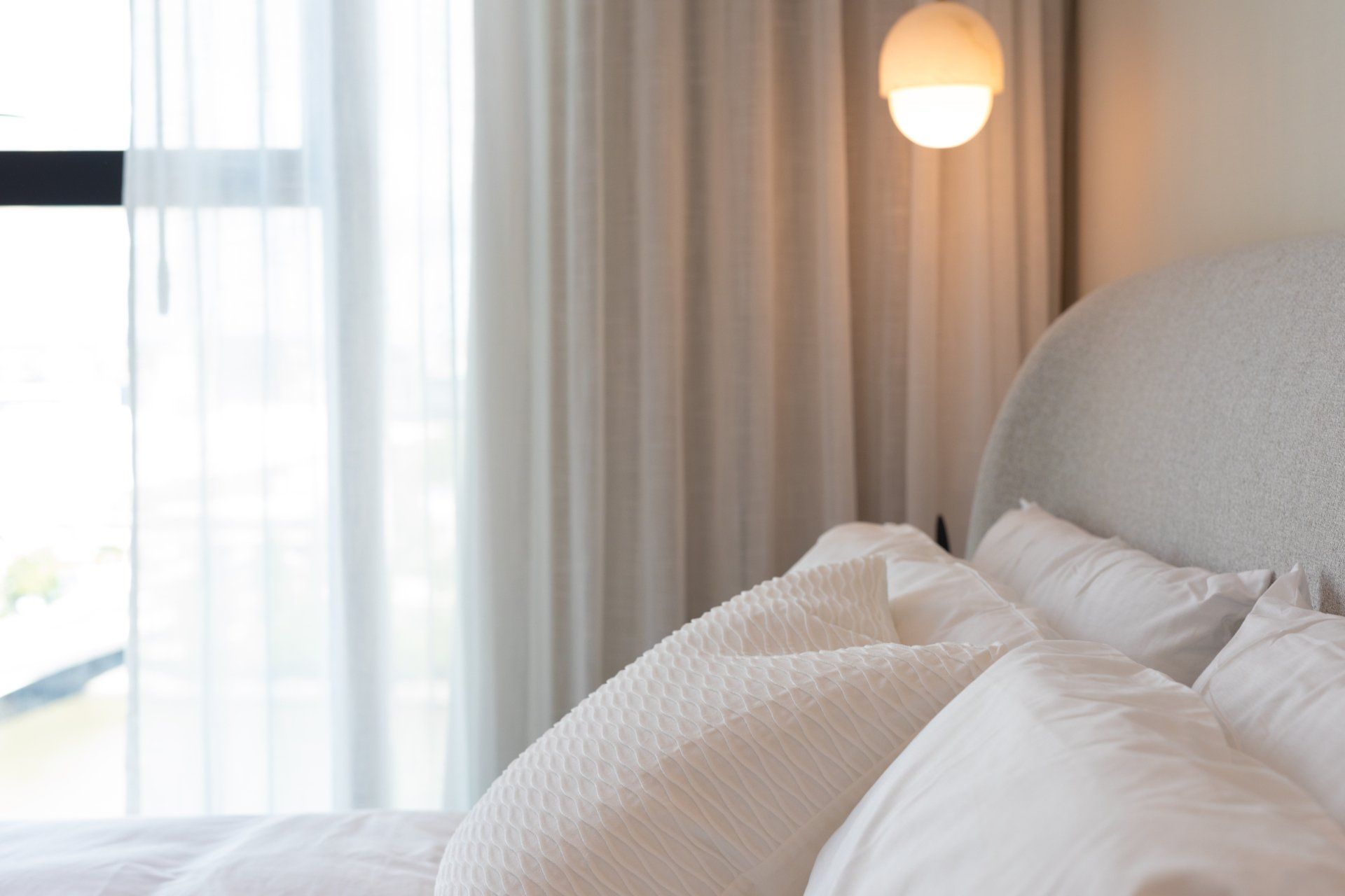 A bed with white sheets and pillows in a bedroom next to a window.