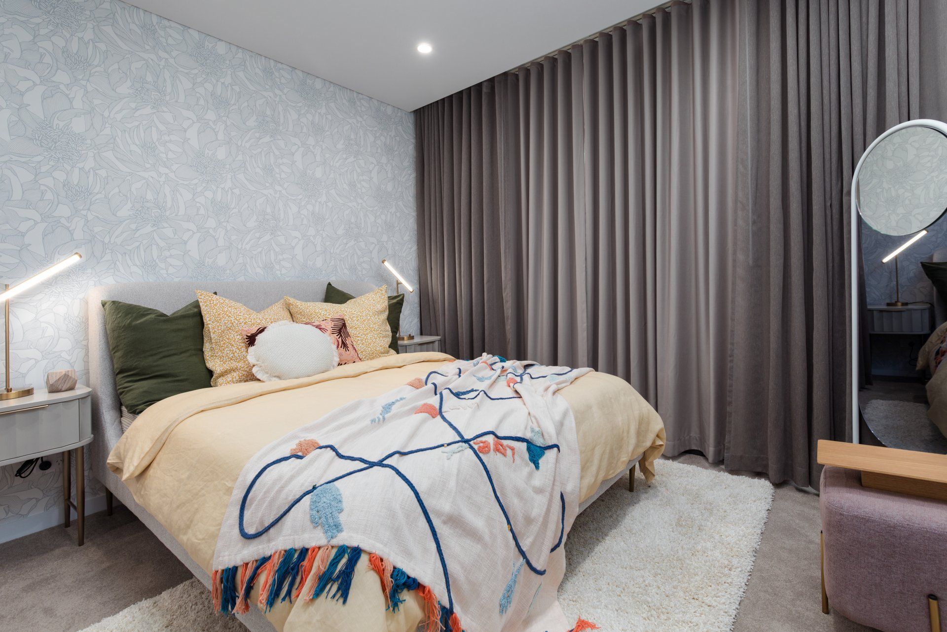 A bedroom with a bed , nightstand , mirror and curtains.