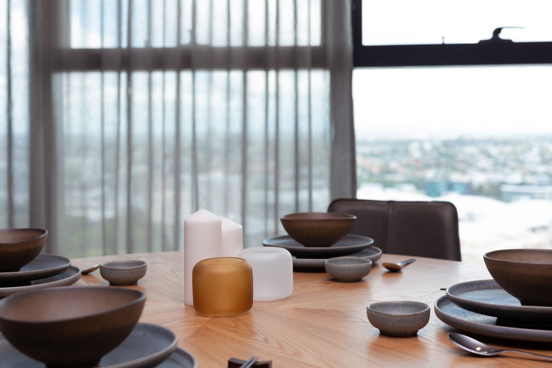 A dining room table with plates , bowls , candles and chopsticks.