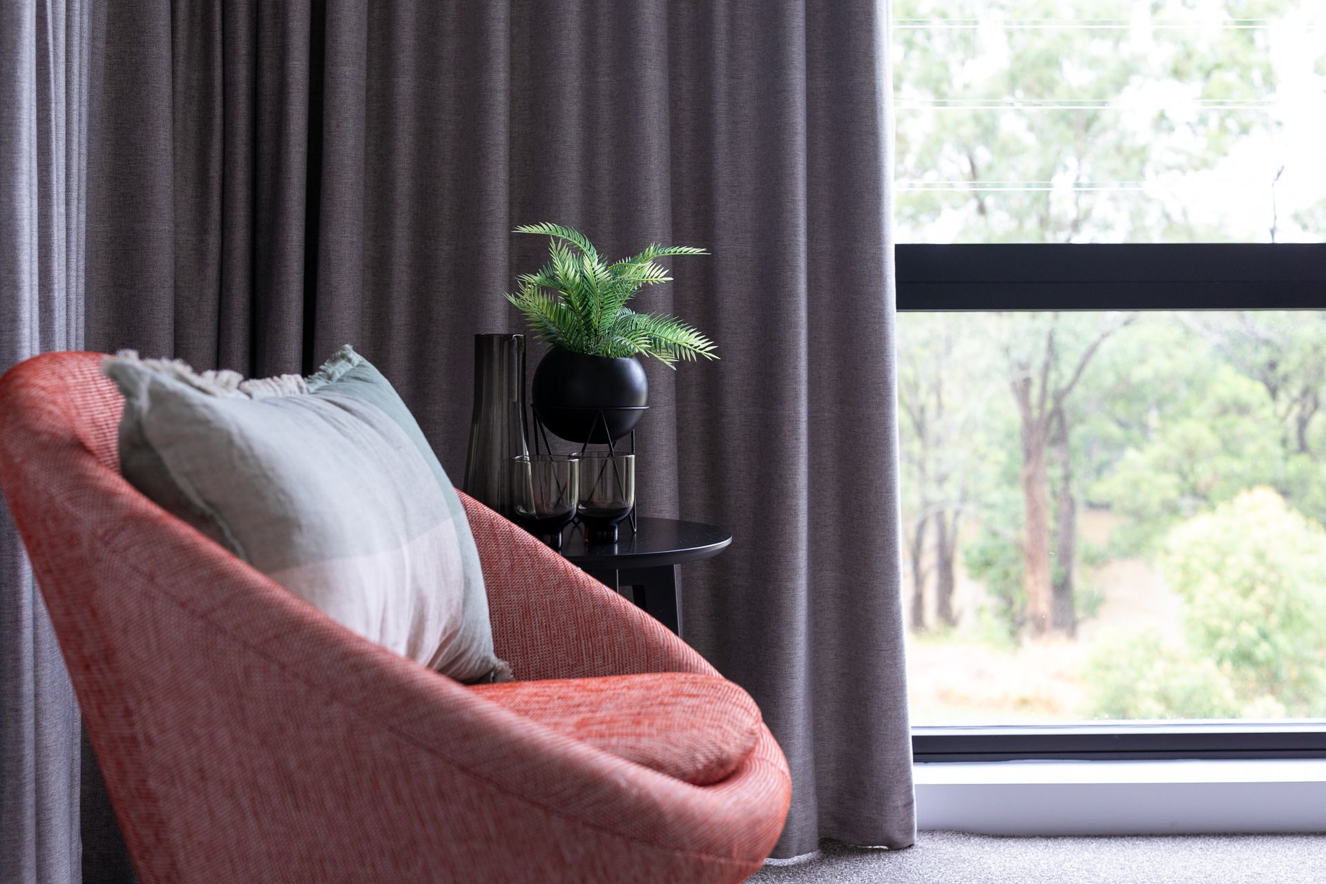A red chair is sitting next to a window in a living room.