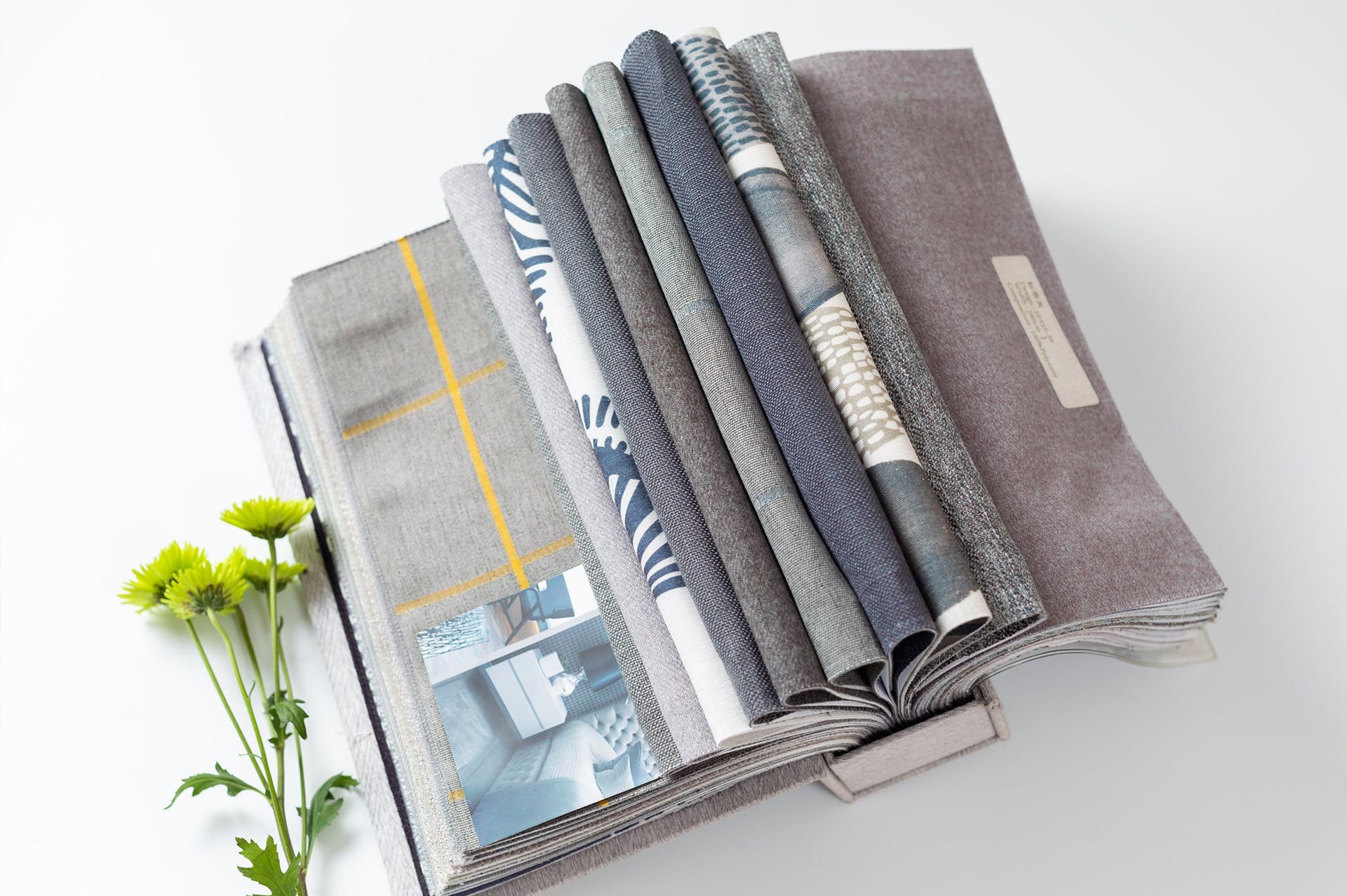 A stack of fabrics is sitting on top of a book next to a flower.