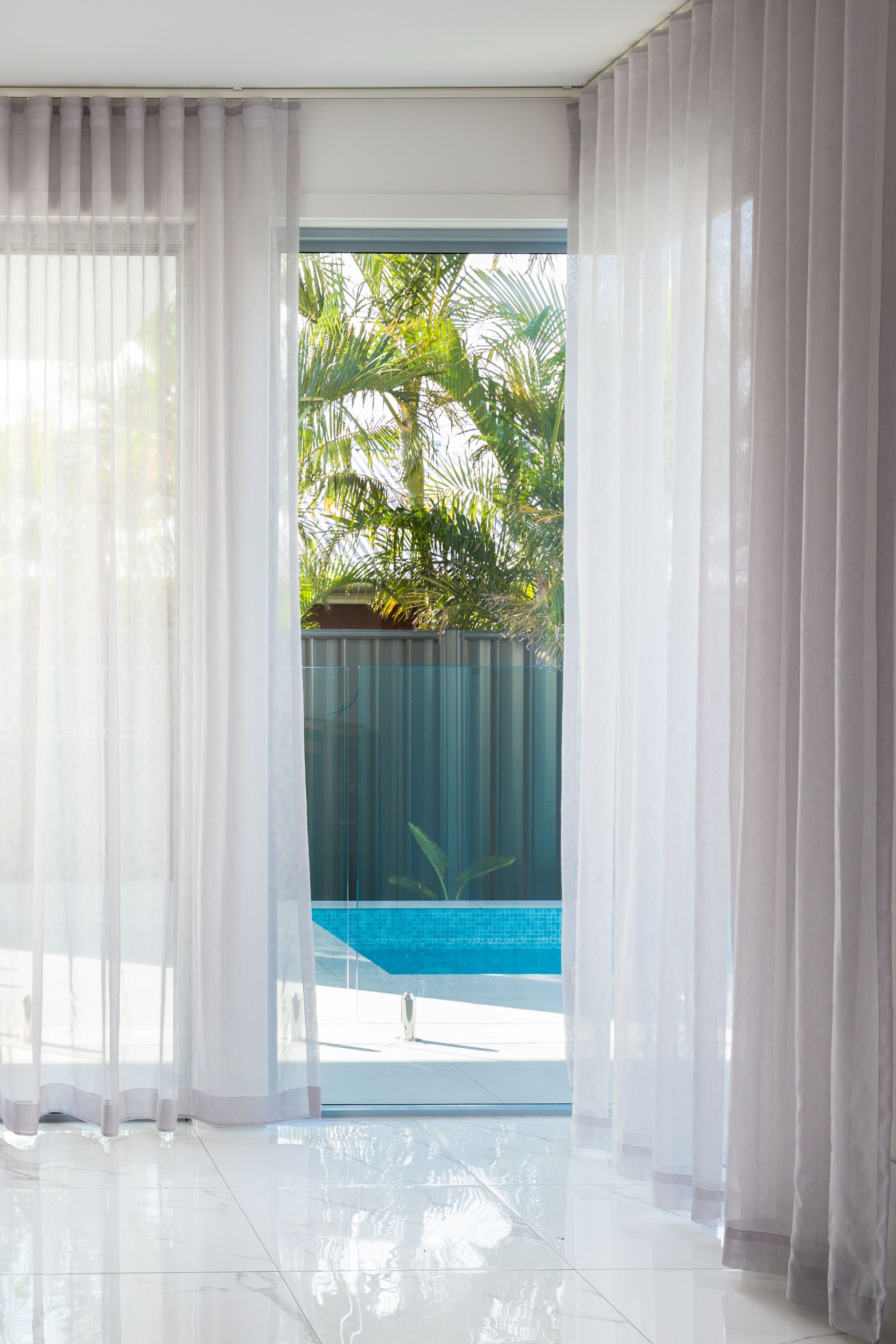 A room with white curtains and a sliding glass door leading to a pool.
