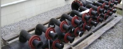 A row of black pipes with red wheels are sitting on a wooden pallet.