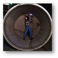 A man is welding inside of a large pipe.