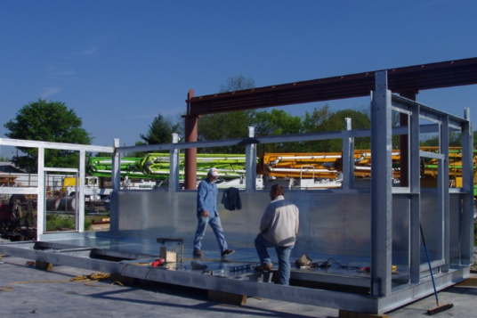 Two men are working on a metal structure with a blue sky in the background