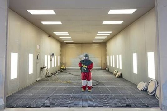 A man in a protective suit is standing in a paint booth.