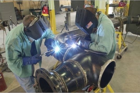 Two men are welding a pipe in a factory