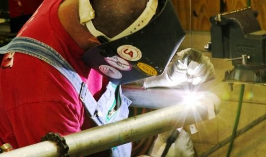 A man wearing a welding mask is welding a pipe