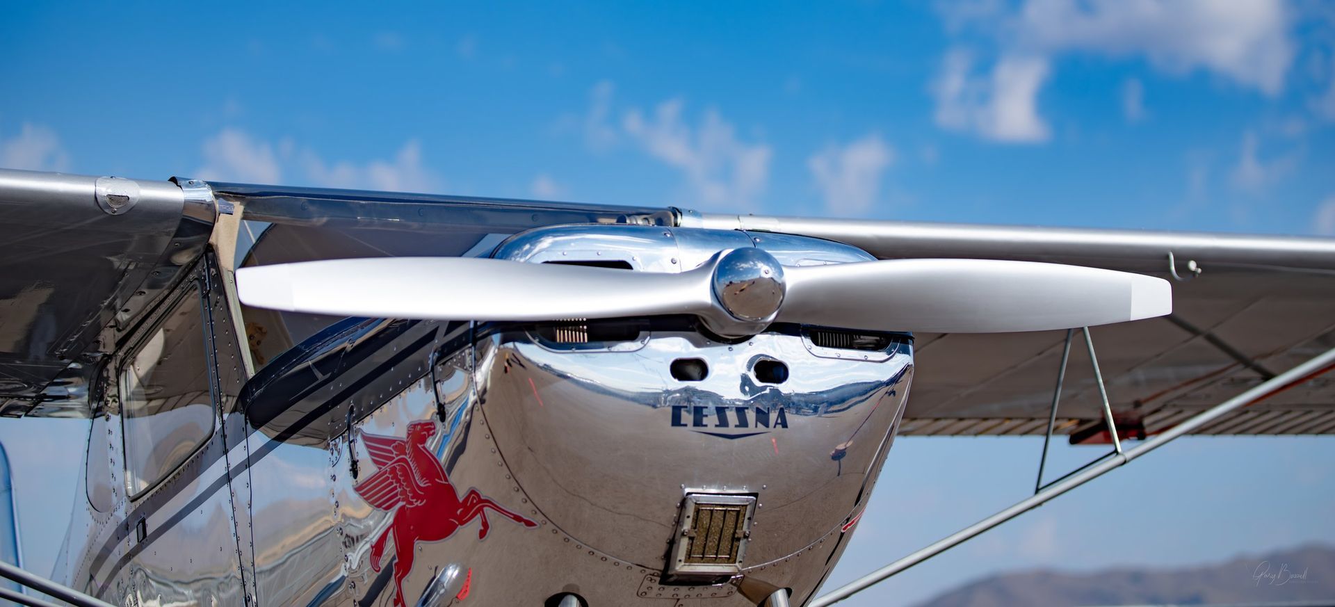Front view of a small white propeller airplane on a runway under a clear blue sky