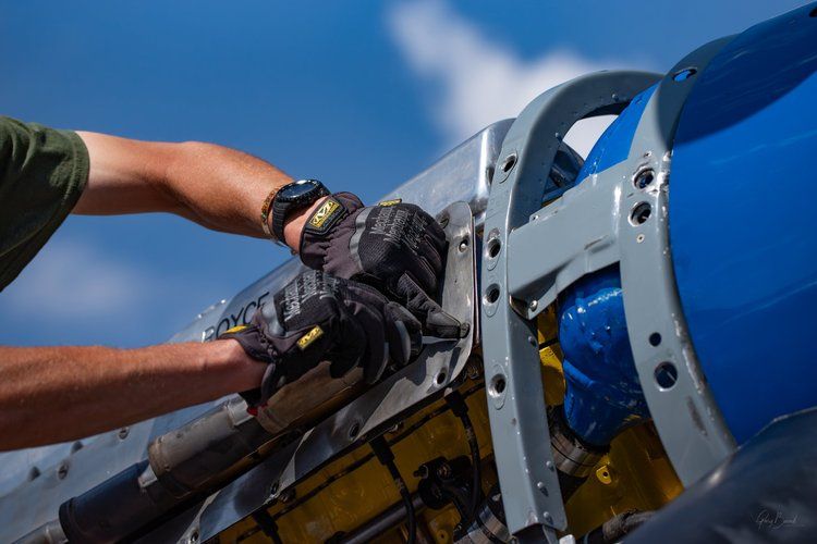 Hands using a wrench on blue and silver metal machinery outdoors against a blue sky