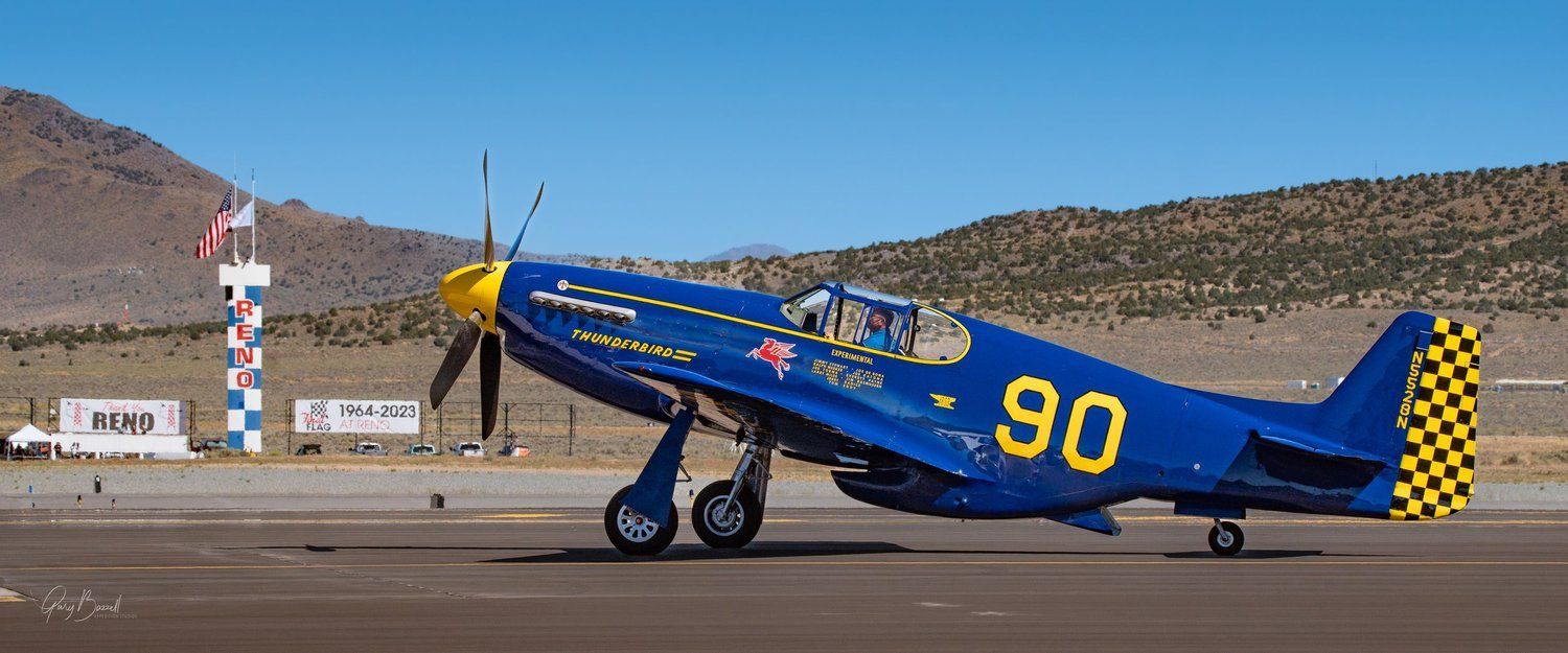 Blue vintage airplane with yellow markings on a runway, propeller spinning
