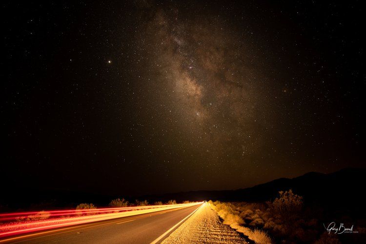 Night road with red light trails under a starry sky and visible Milky Way.