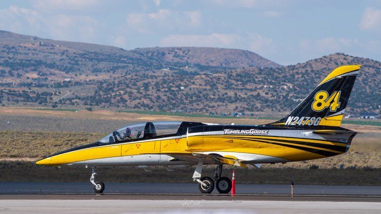 Yellow-and-black jet parked on a runway with mountains in the background, number 84 on the tail