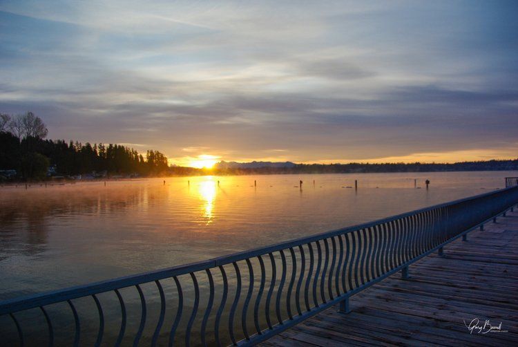 Sunset over a calm lake with a long boardwalk railing in the foreground